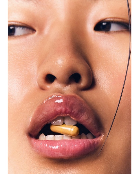 An extreme, high-detail macro shot of a model holding a golden capsule between her teeth to create a sensory, product-centric hook.